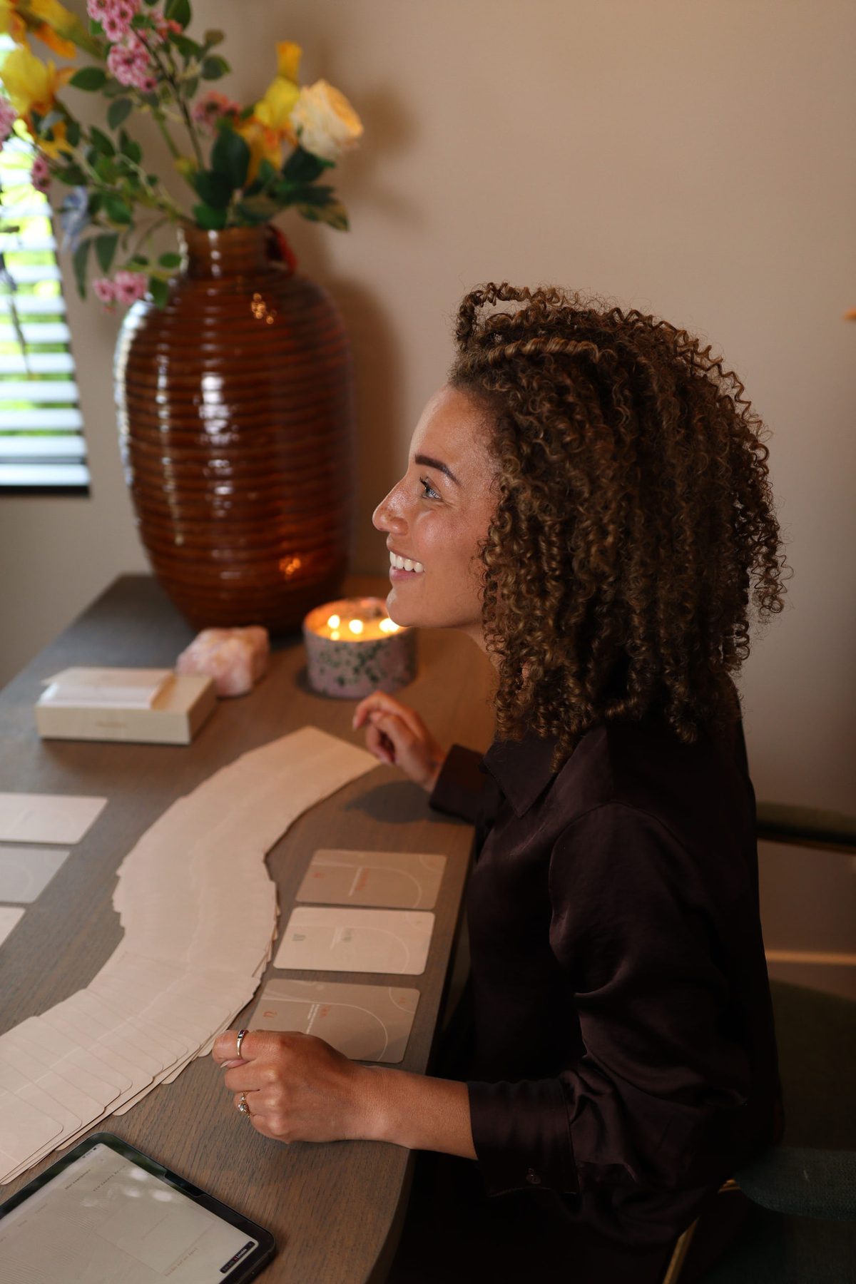 Sushila lachend aan tafel tijdens een sessie, met kaarten voor zich
